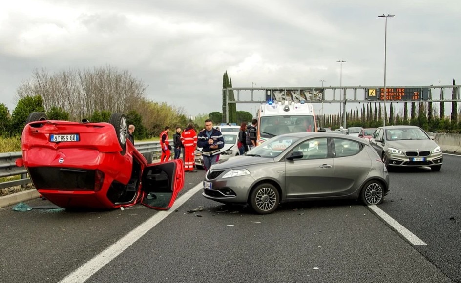 Car turned upside down, surrounded by ambulance, police officer and people