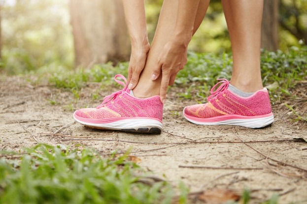 Woman runner holding her twisted ankle after running exercise outdoors