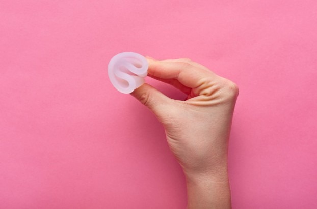 Close up view of woman holding menstrual cup isolated over rose, woman's period
