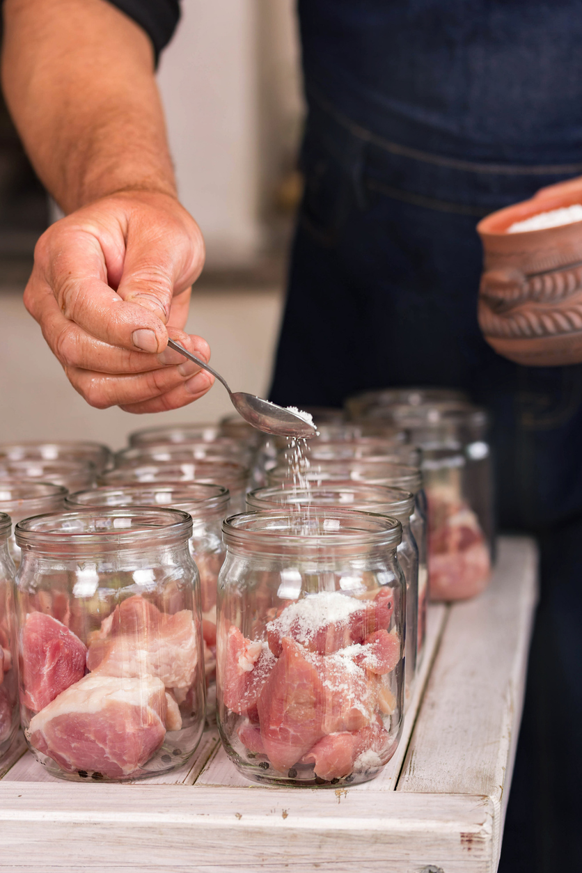 Man hand pours salt in a jar of meat