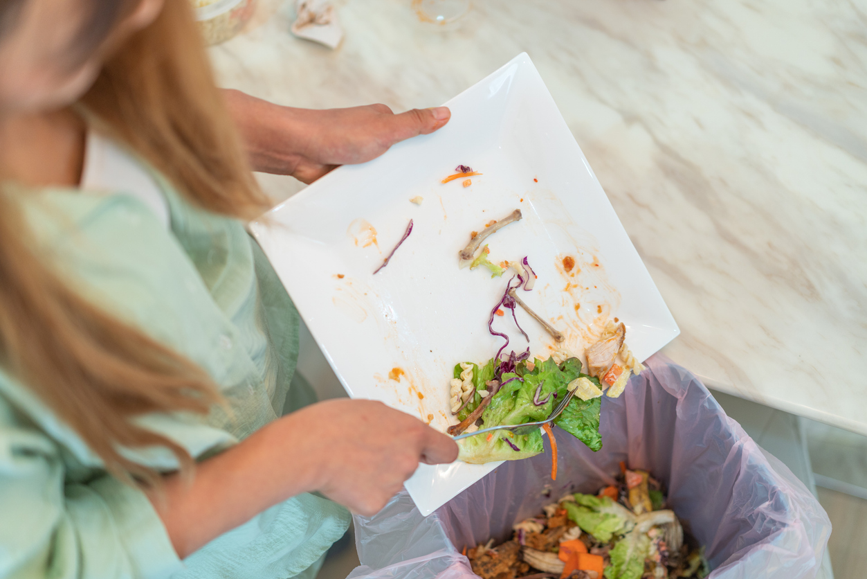 A women putting leftovers into a bowl before throwing them into a garbage bin