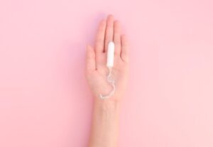 Hand holding tampon on pink background
