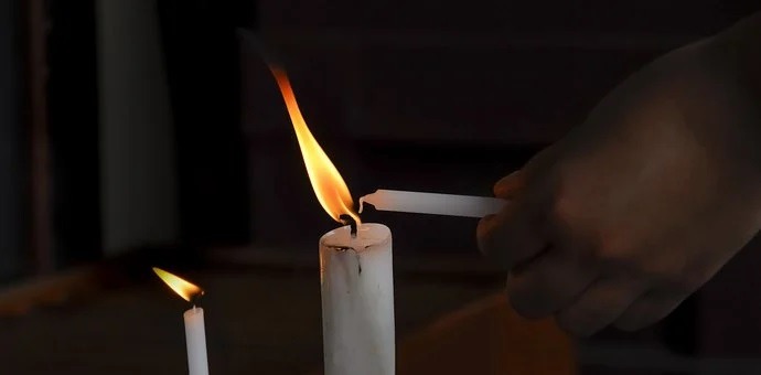 Person lighting candle using the flame of another candle
