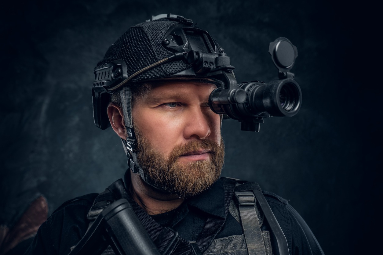 Close-up portrait of a bearded special forces soldier observes the surroundings in night vision goggles.